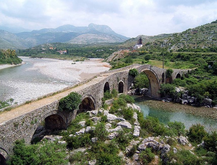 The stone arches of Mesi Bridge over the Kir river near Shkodra, with mountains behind