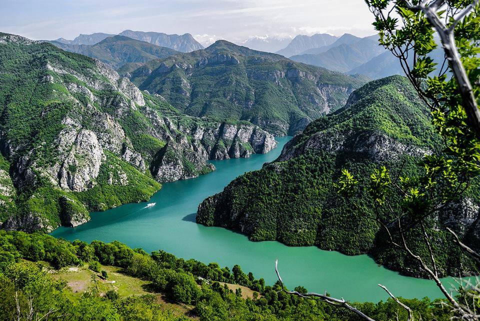 Turquoise water of the Vau i Dejes reservoir winding between steep green mountains