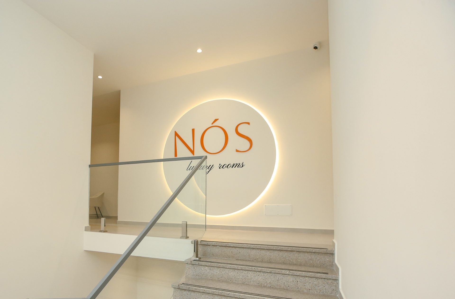 Backlit NÓS luxury rooms logo above the staircase inside the boutique hotel in Shkodër